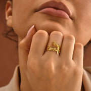 Close-up of a hand wearing a 14k gold filled birth flower name ring with 'Jennifer' on it, against a blurred background.